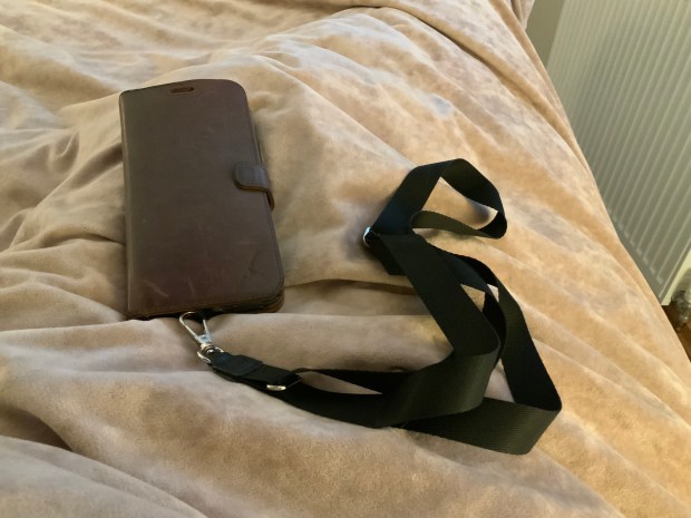 A brown leather phone case and a black strap on a beige blanket.