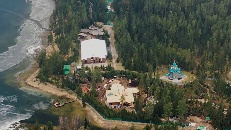 Aerial view of a large estate under construction, near a lake and forest, with a church visible.