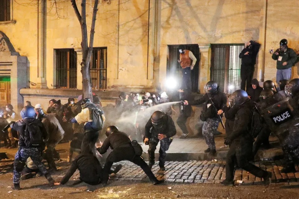 Police in riot gear using pepper spray against protesters.