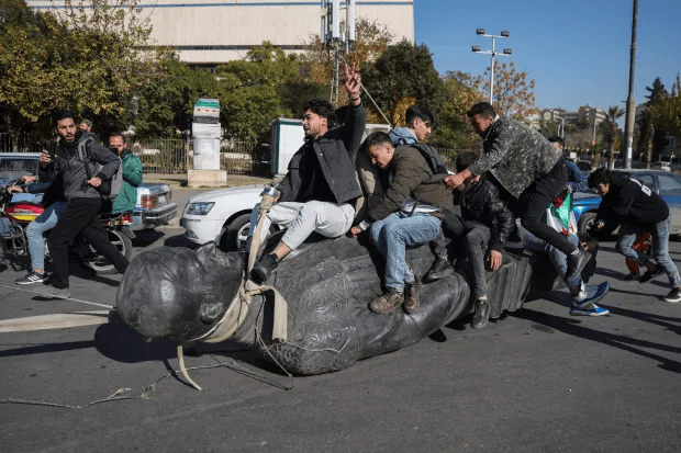 Syrians ride on a statue of Hafez