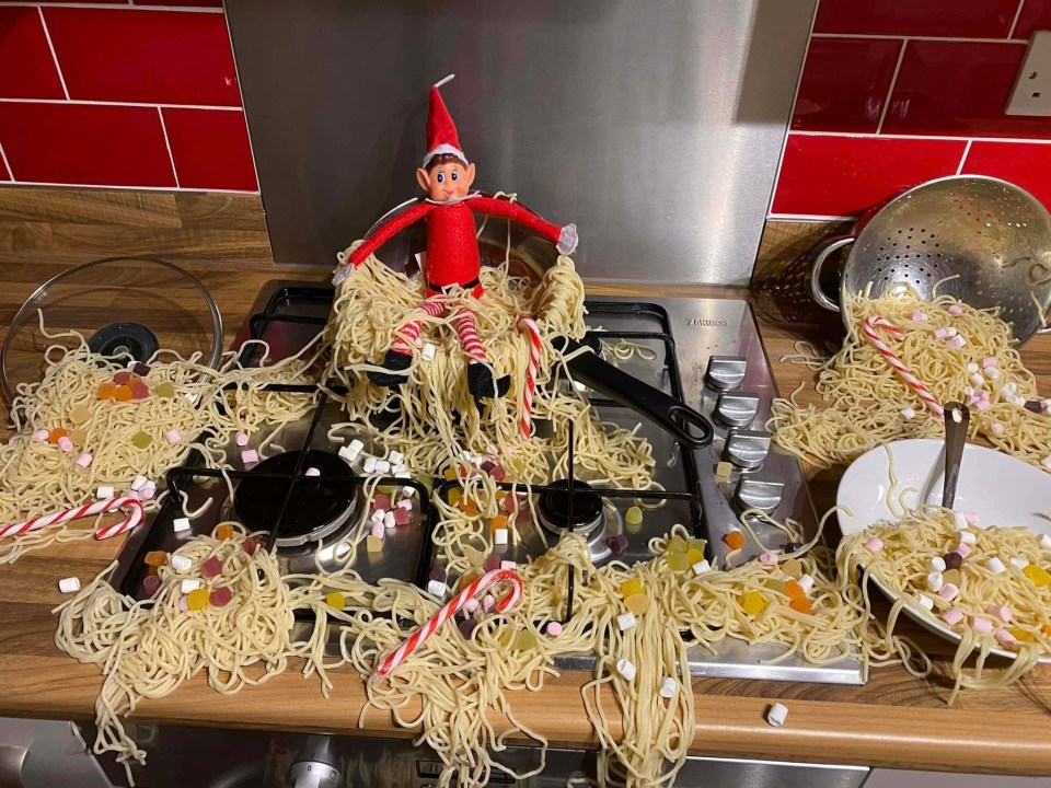 Elf on the Shelf in a pot of spaghetti and sweets on a kitchen counter.