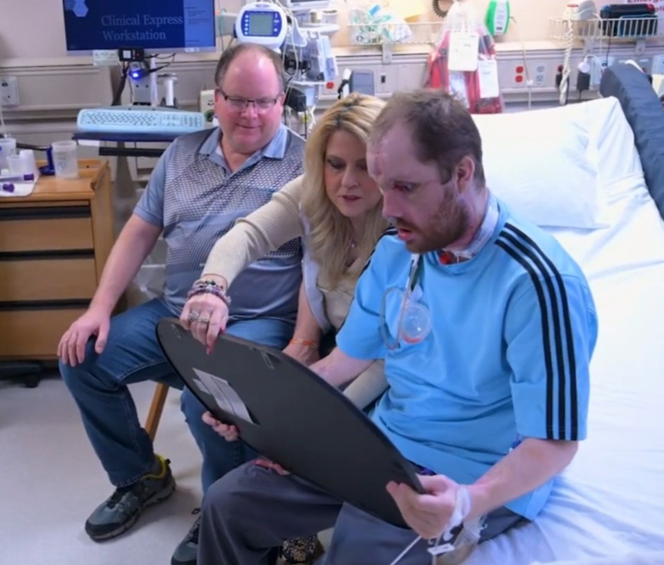 Man in hospital bed looking at a mirror with his parents.