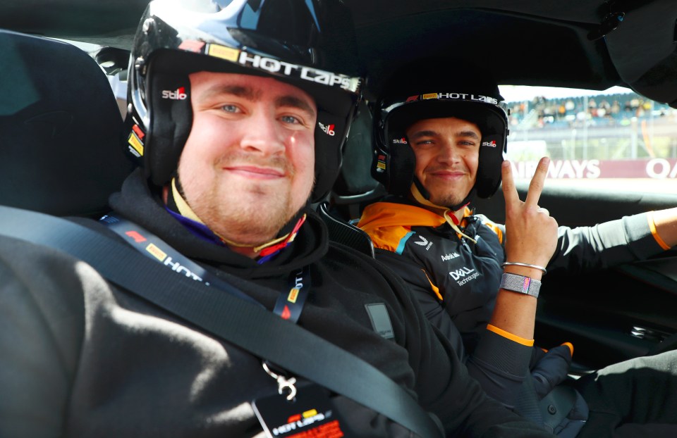 Lando Norris and another person in racing helmets and gear inside a car at Silverstone Circuit.