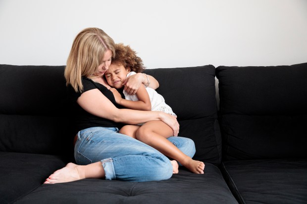 A mother comforting her young daughter on a couch.