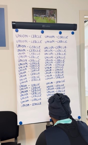 A whiteboard with the phrase "UNION - CERCLE" repeatedly written on it.  A person is looking at the board.