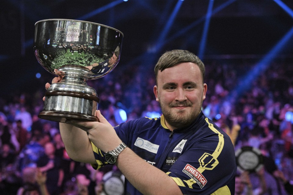 Luke Littler holding the Eric Bristow Trophy.