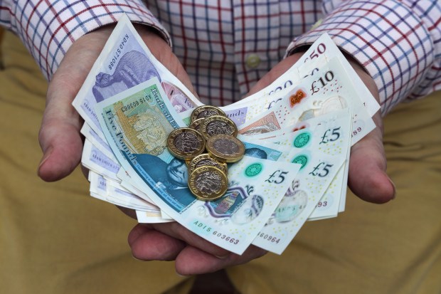 Hands holding British pound coins and banknotes.