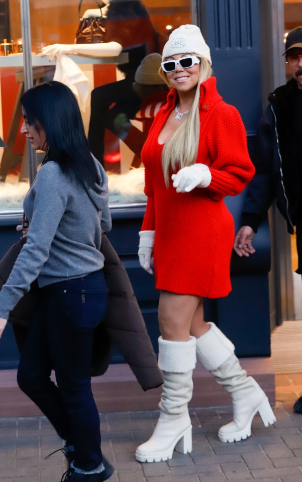 Mariah Carey in Aspen wearing a red sweater dress, white boots, and sunglasses.