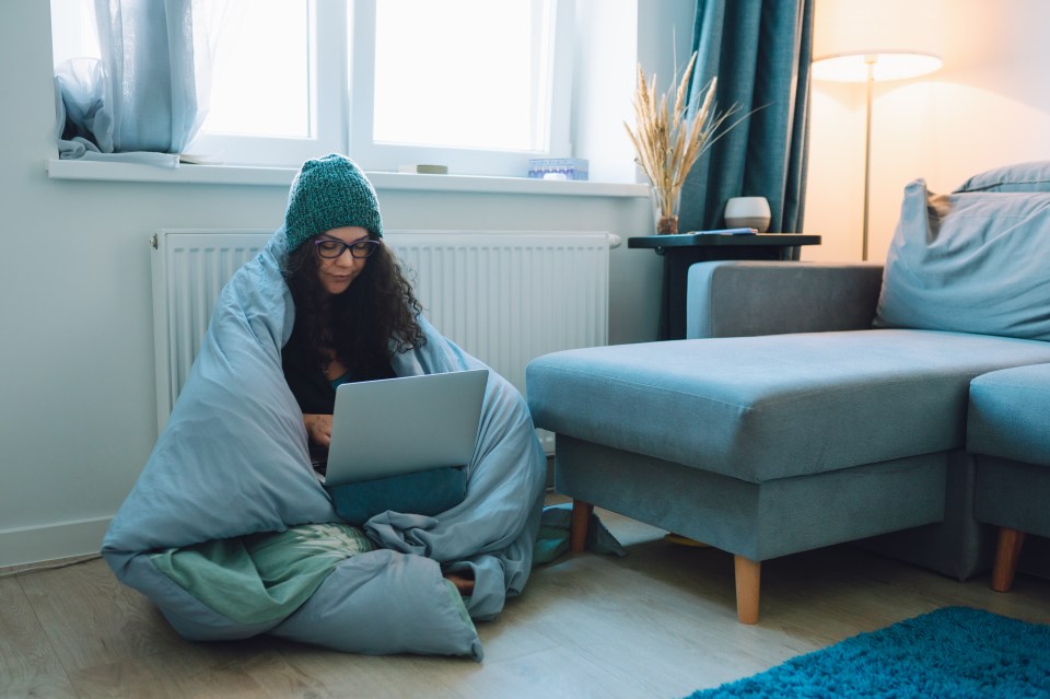 Woman working on laptop at home, wrapped in a blanket to stay warm.