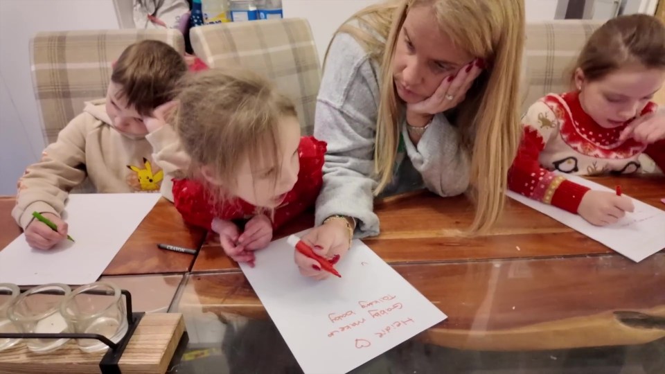 A group of children writing on a piece of paper, likely making Christmas present lists.