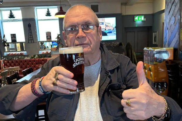 Man in pub giving thumbs up, holding pint of John Smith's beer.