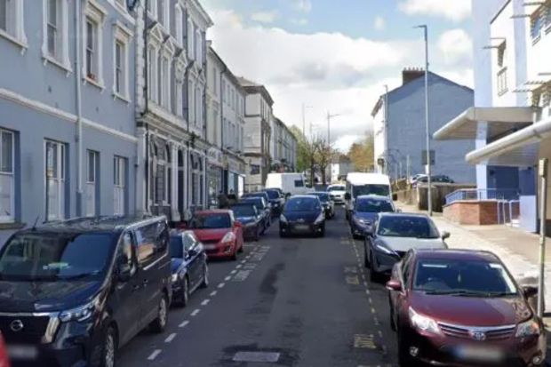 Cars parked on both sides of a narrow street lined with buildings.