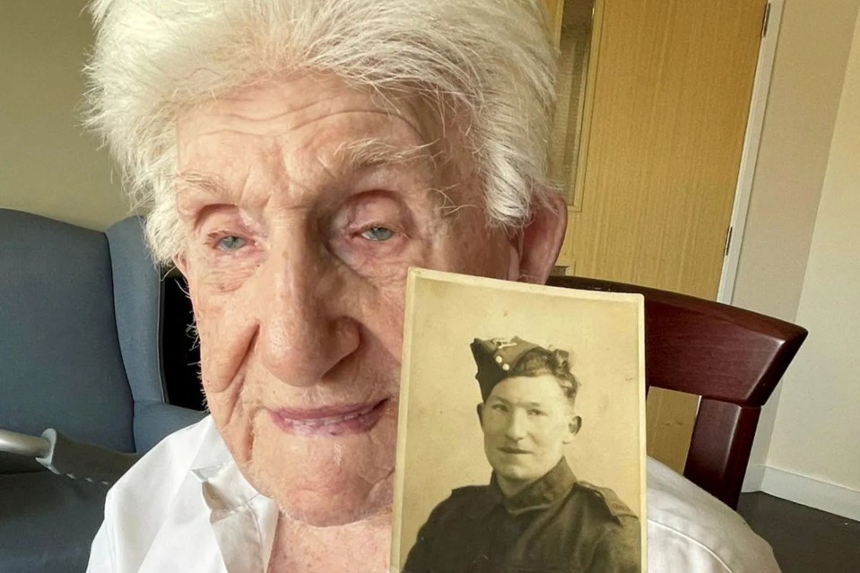 Elderly woman holding a photo of a young man in military uniform.