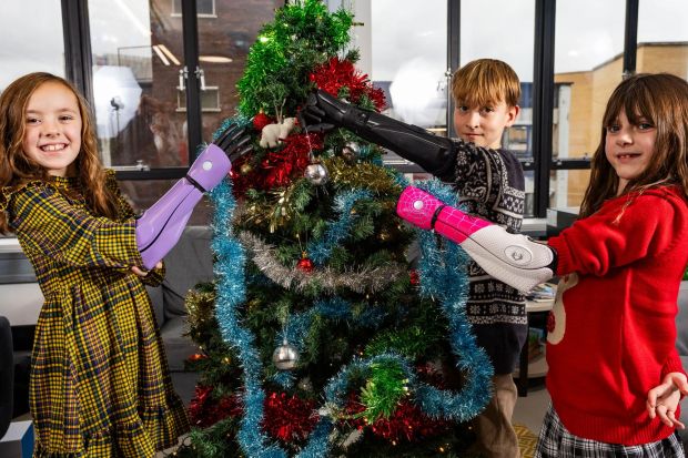 Three children with prosthetic arms decorate a Christmas tree.