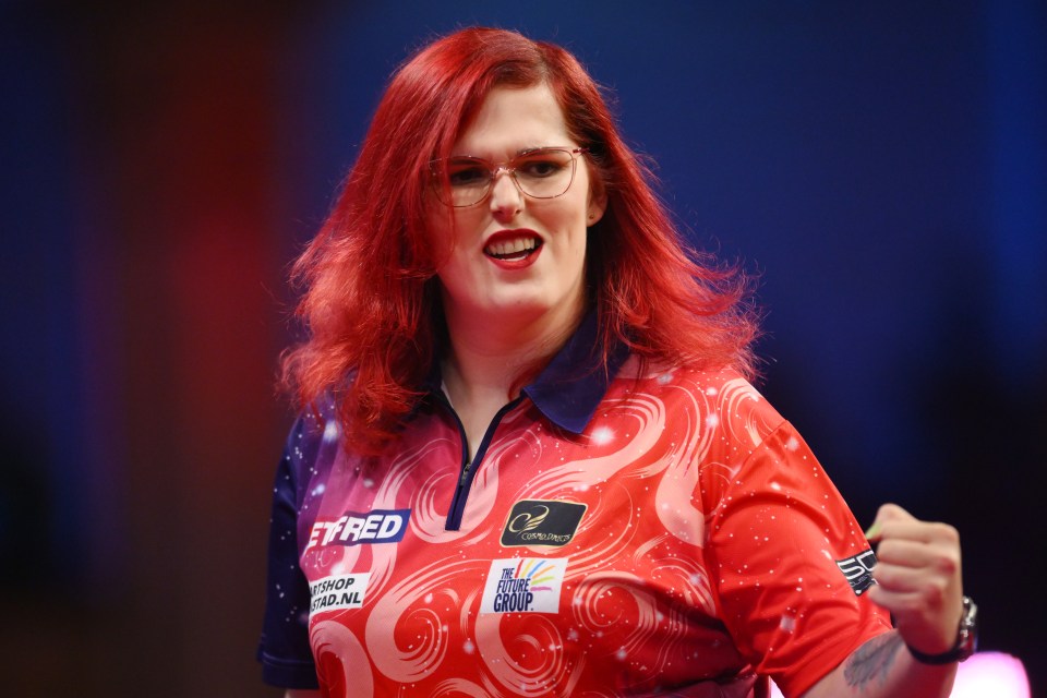 A woman celebrating her darts win, raising her hands in the air.
