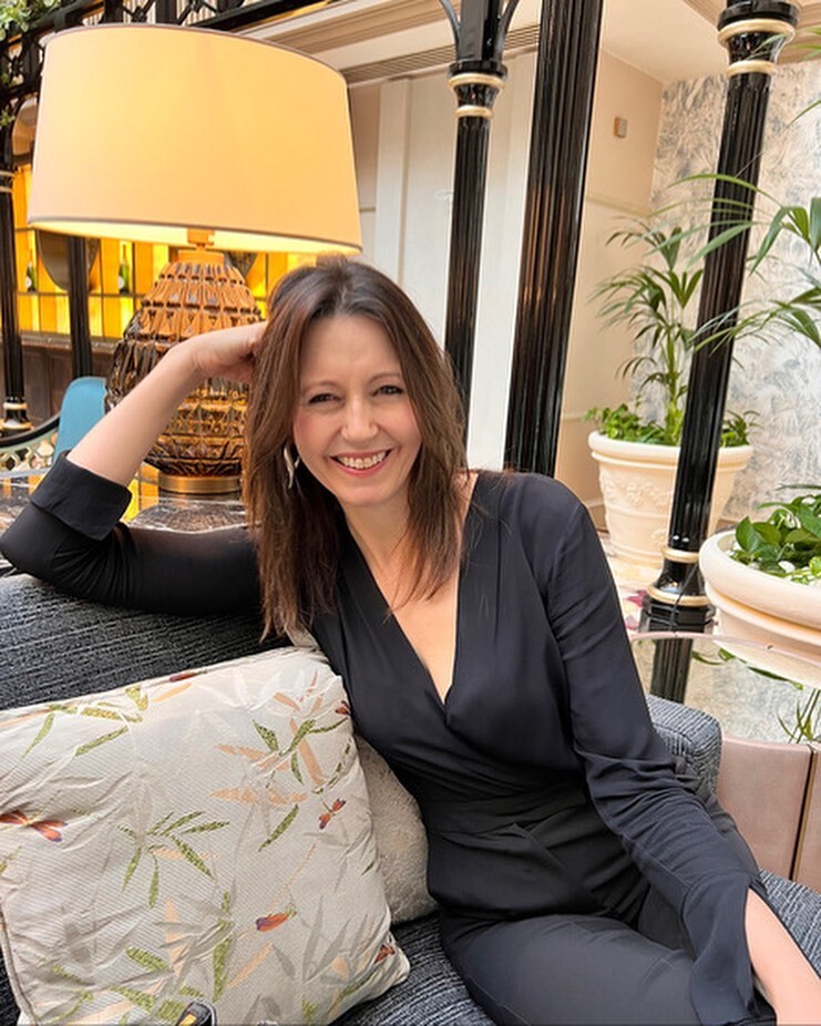 Woman in black jumpsuit sitting on a couch.