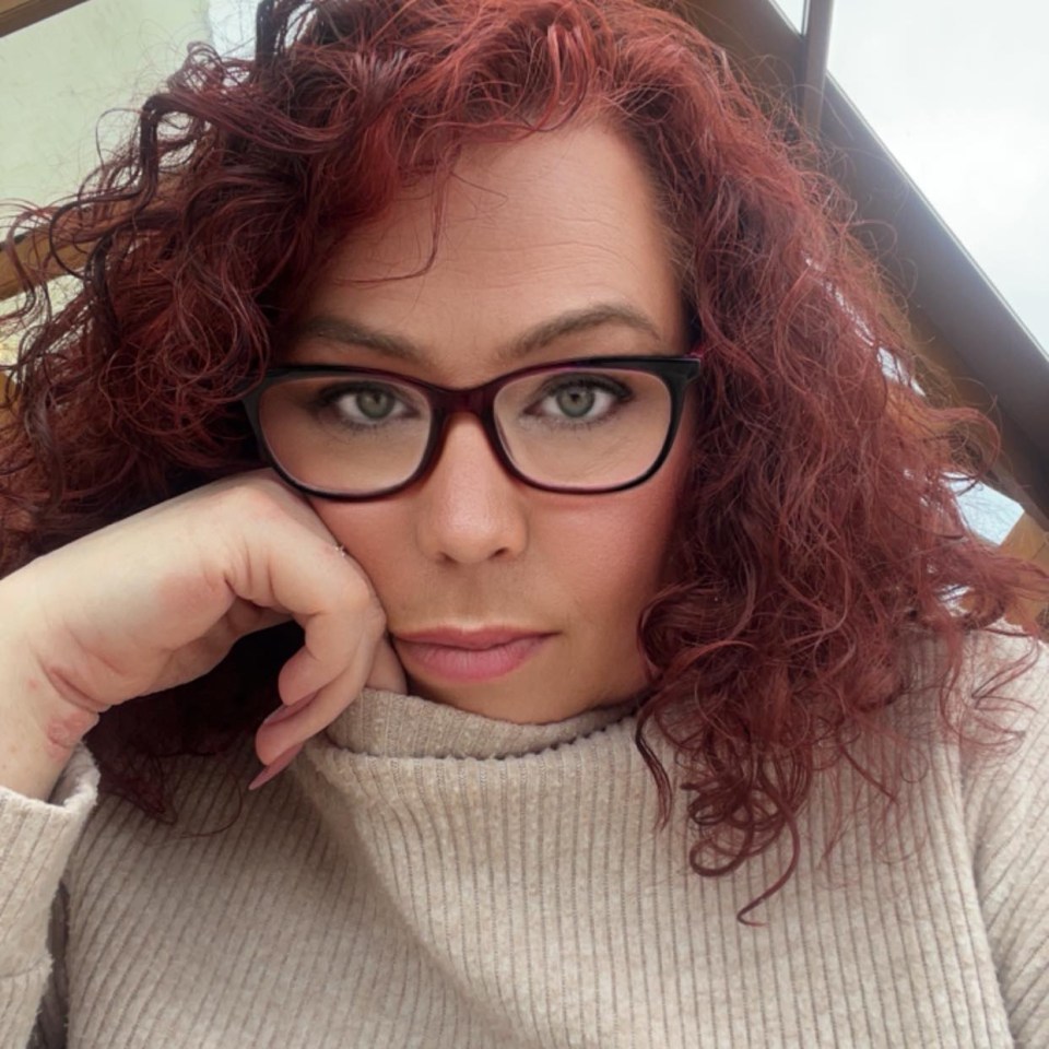 Portrait of a woman with red curly hair wearing glasses.