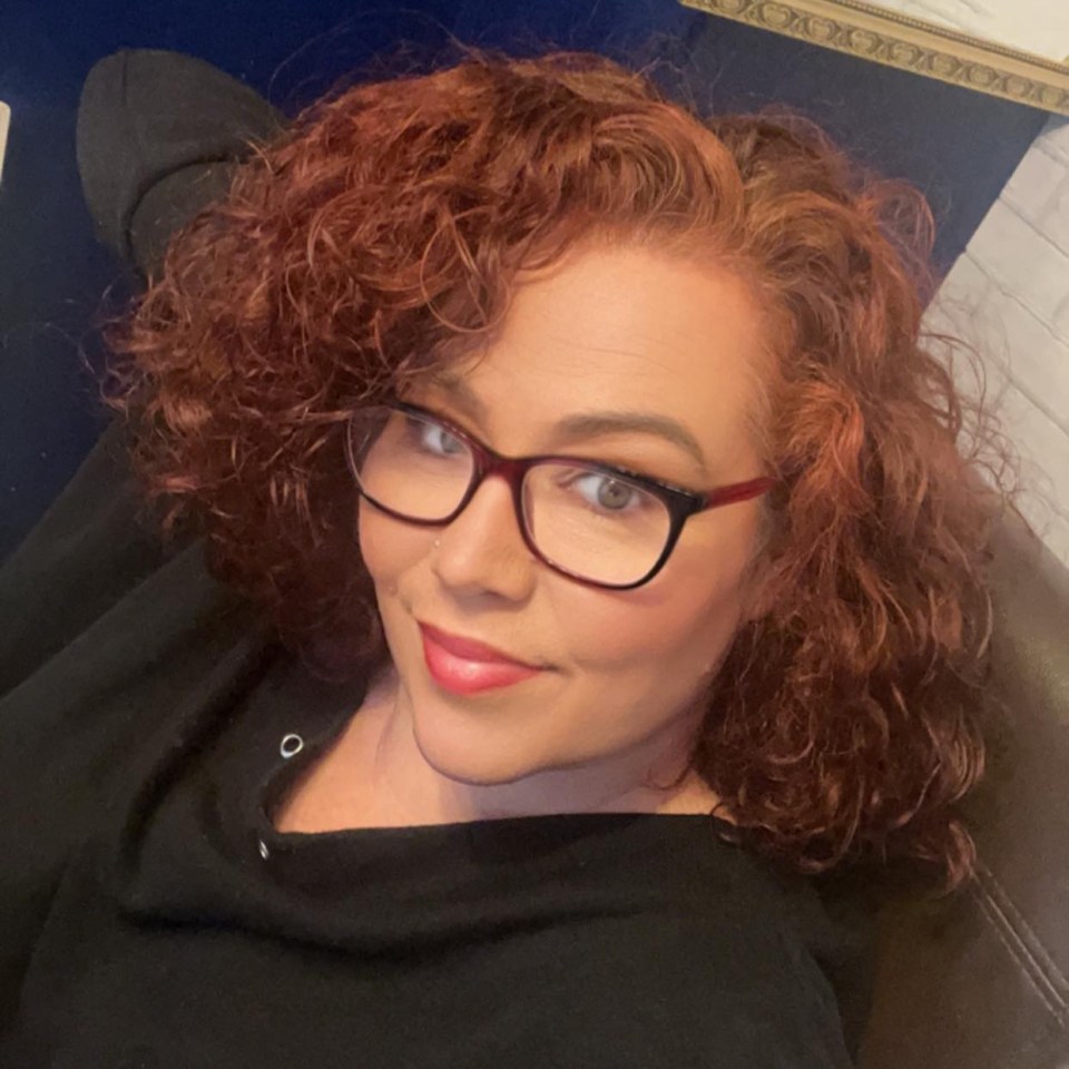 Headshot of a woman with curly auburn hair wearing glasses.