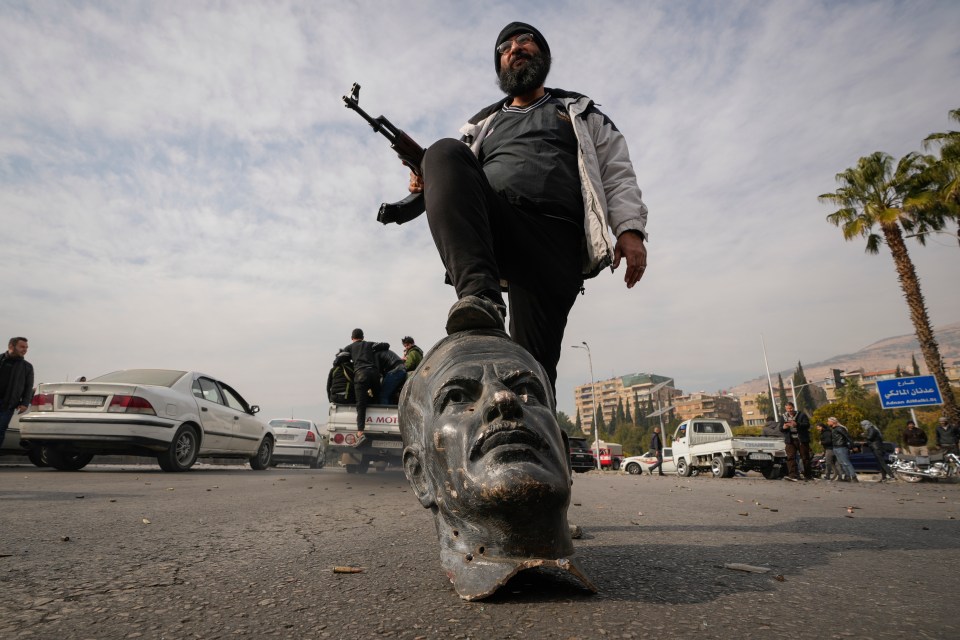 An opposition fighter steps on a broken bust of Assad's father and former president Hafez