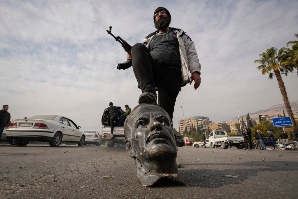 An opposition fighter steps on a broken bust of the late Syrian President Hafez Assad in Damascus