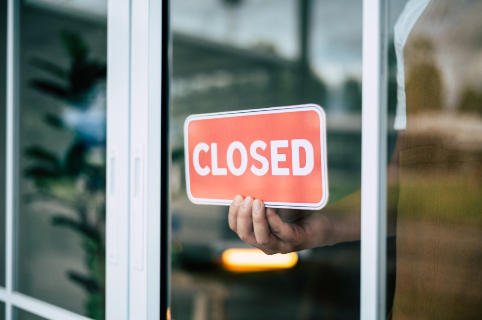 Person placing a "Closed" sign on a shop door.