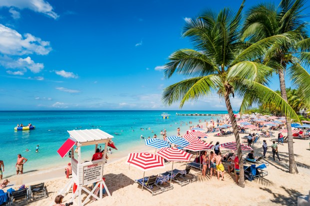 Crowded Doctor's Cave Beach in Montego Bay, Jamaica, with people swimming, sunbathing, and relaxing under umbrellas.