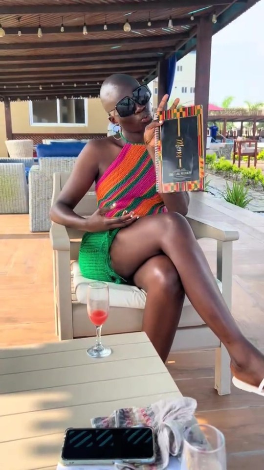 A woman in a colorful crocheted dress holds a menu at an outdoor restaurant.