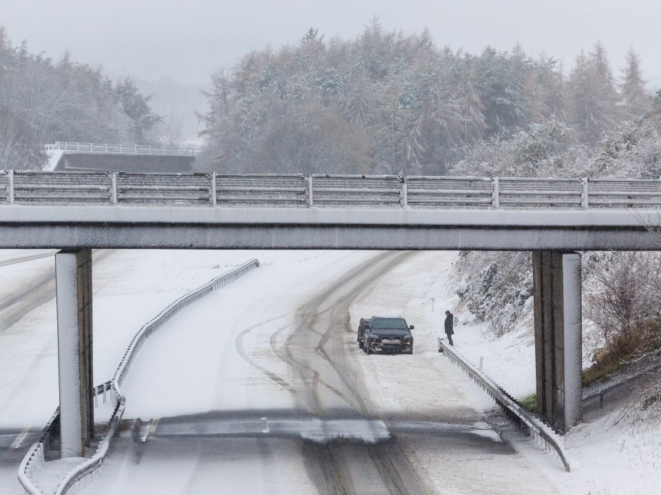 A person stands next to his vehicle on an empty snow covered M9 motorway near Stirling on November 23