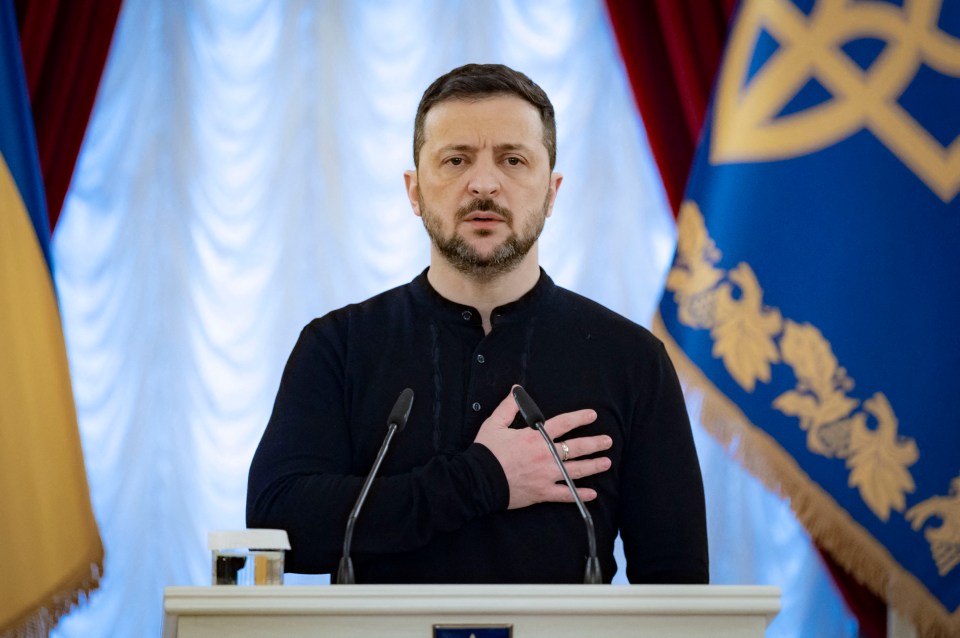 Volodymyr Zelenskyy stands at a podium, hand on heart, during a ceremony in Kyiv.