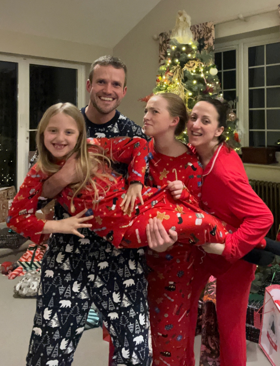 Family in matching Christmas pajamas in front of a Christmas tree.