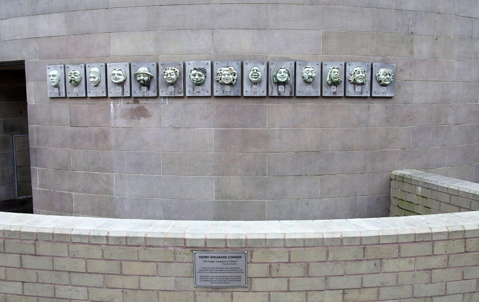 Derby Speakers Corner: A wall with mounted ceramic faces and an informational plaque about free speech.