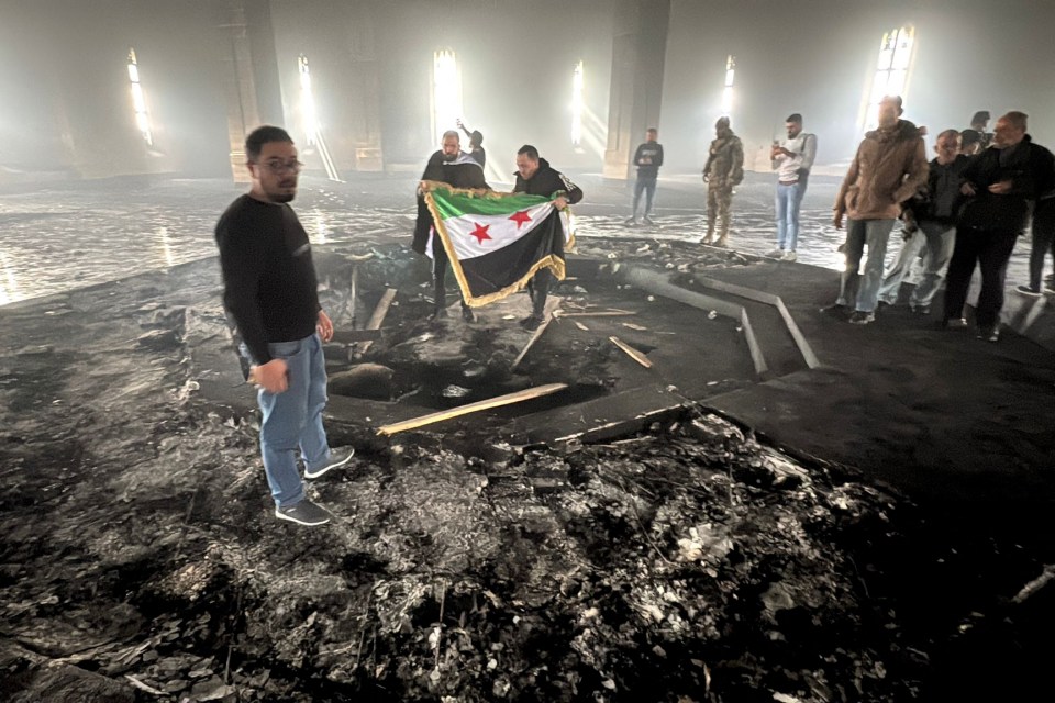 Rebel fighters stand with the flag of the revolution on the burnt gravesite of Syria’s late president Hafez al-Assad