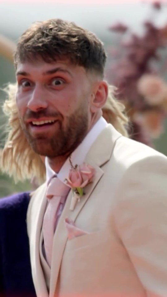 A shocked groom in a beige suit at a wedding.