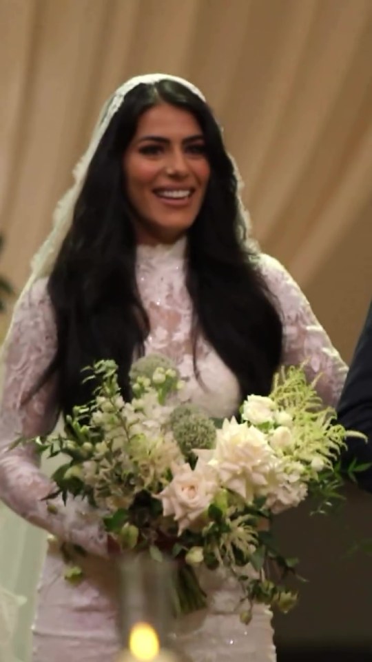 Bride smiling, holding bouquet in lace wedding dress.