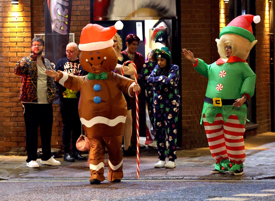 People in Christmas costumes on a city street at night.