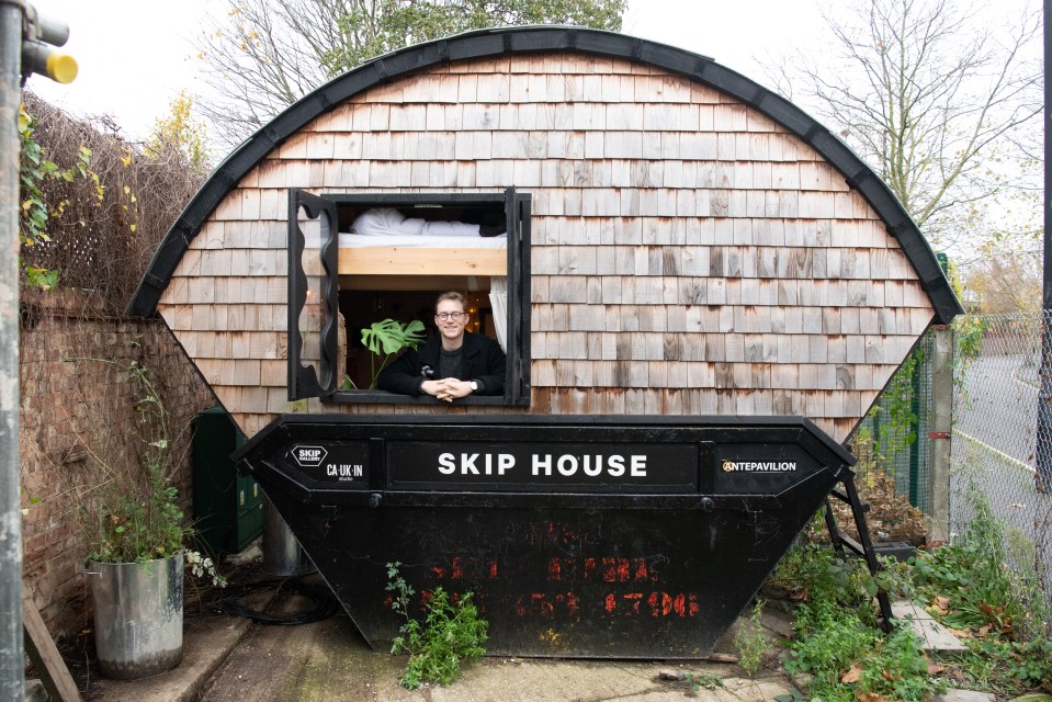 Man smiling in the window of his skip house.