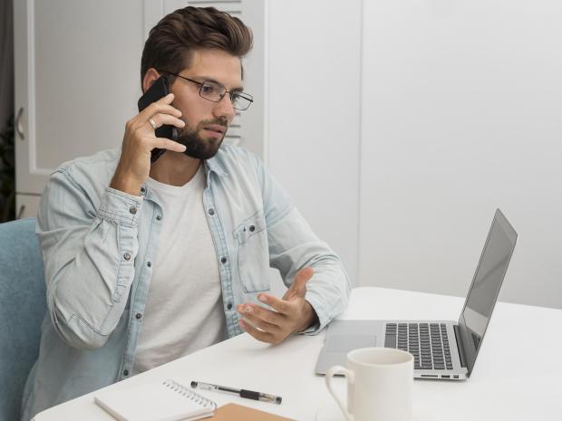 Man on phone call, gesturing at laptop.