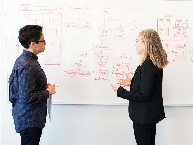 Two people reviewing website designs and marketing plans on a whiteboard.