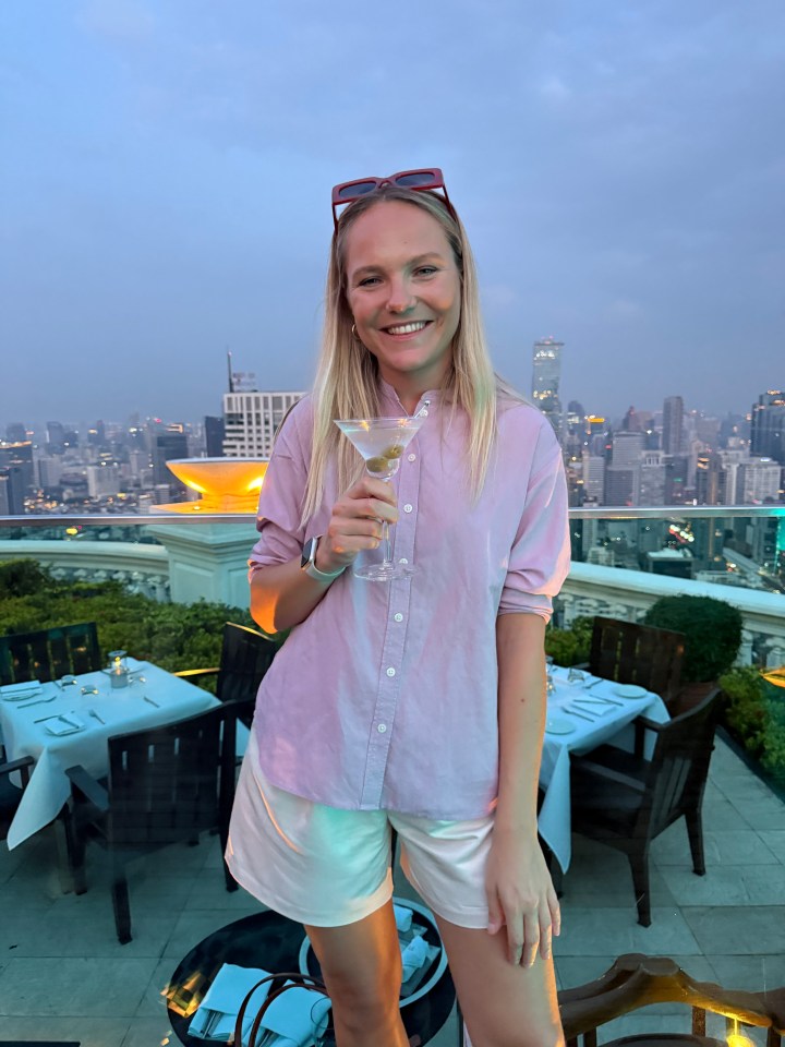 Woman enjoying a martini at a rooftop bar overlooking a city skyline.