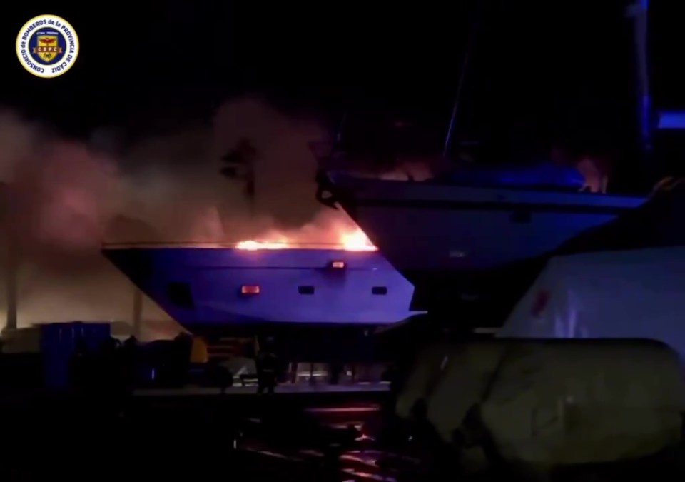 A superyacht engulfed in flames at a port.