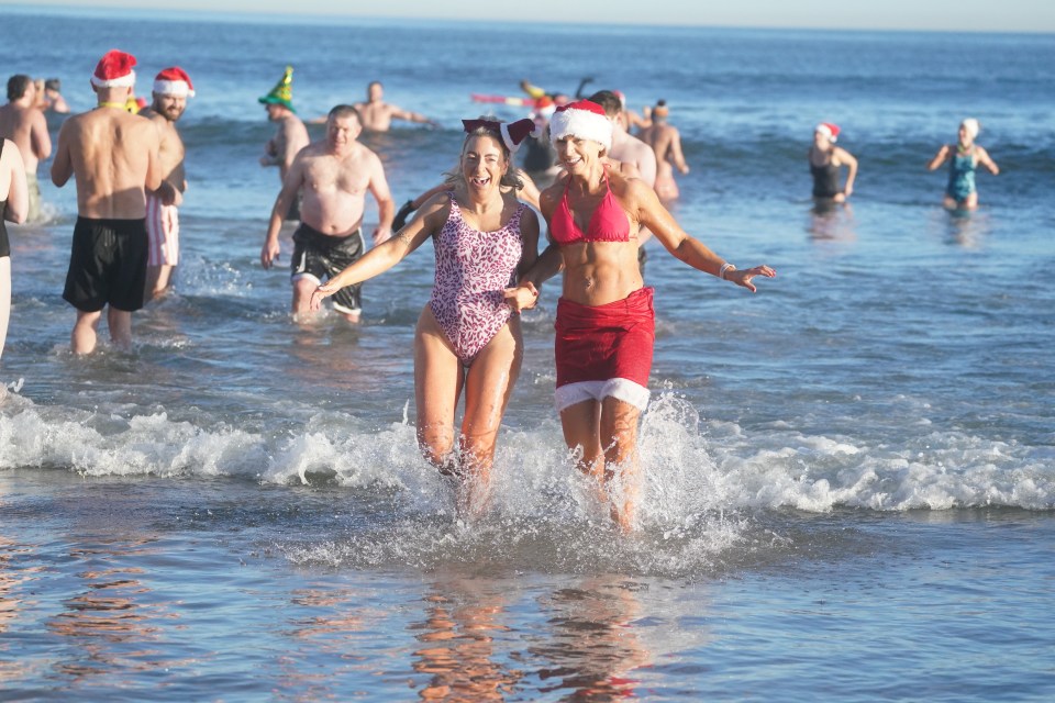 Two women in swimsuits and Santa hats participate in a Boxing Day swim.