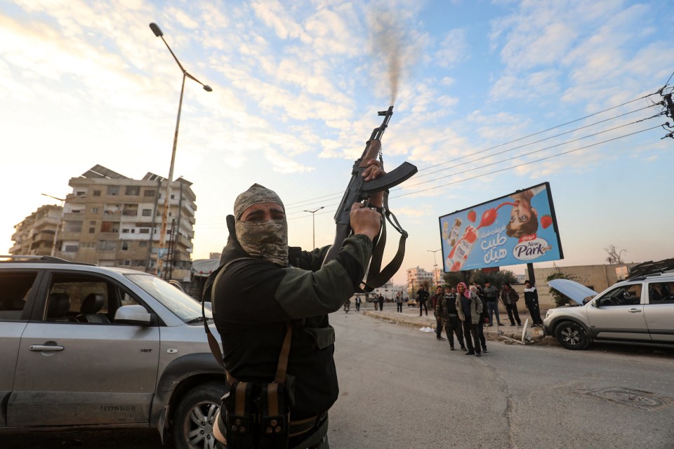 A Syrian rebel fighter fires his rifle into the air in the streets of Hama