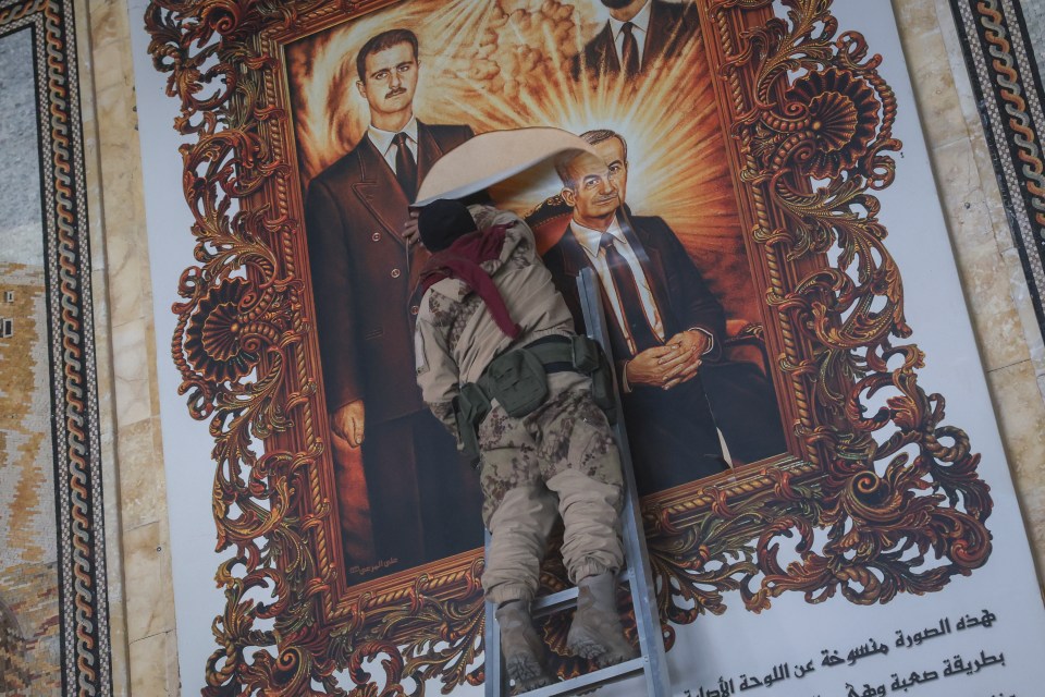 A Syrian opposition fighter tears a painting depicting Assad and his late father