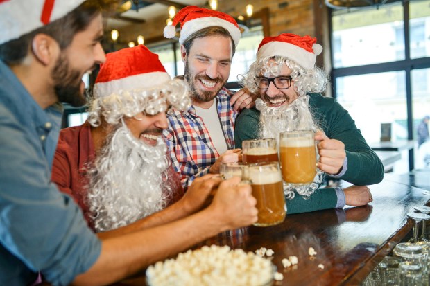 Four men dressed as Santa Claus toast with beer in a pub.