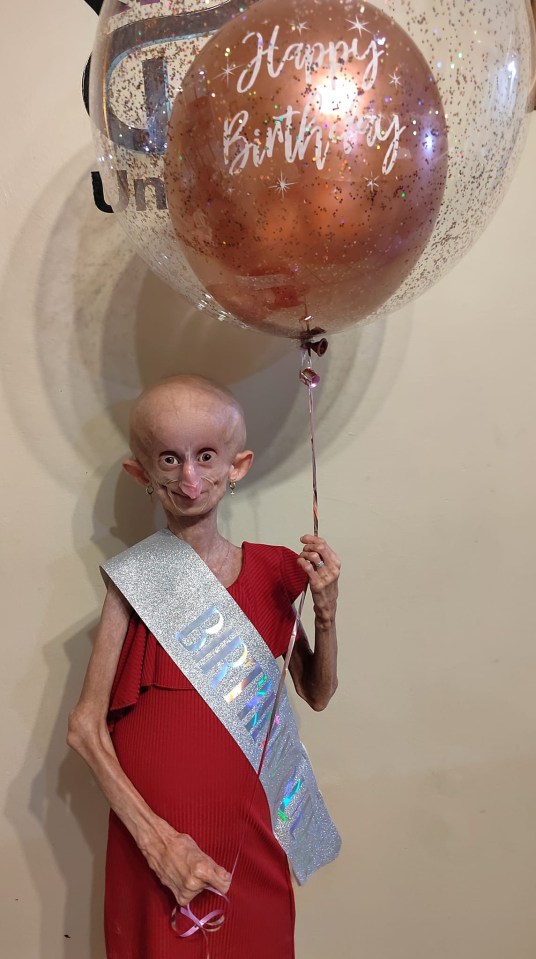 Woman in red dress holding a birthday balloon and wearing a birthday sash.