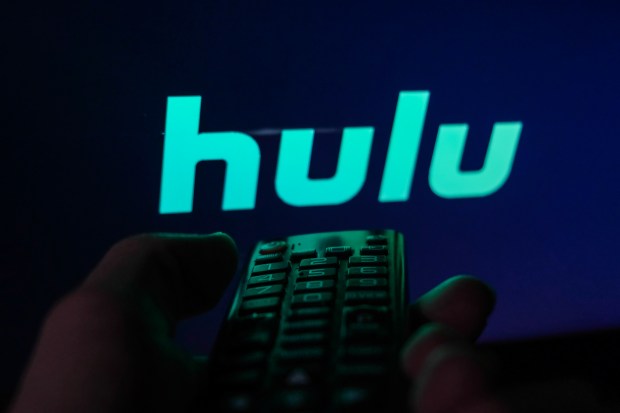 Hand holding a remote control with the Hulu logo on a TV screen.