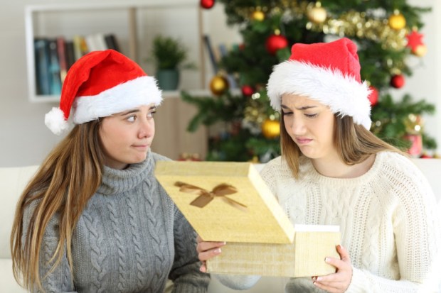 Two women wearing Santa hats look disappointed at a Christmas gift.