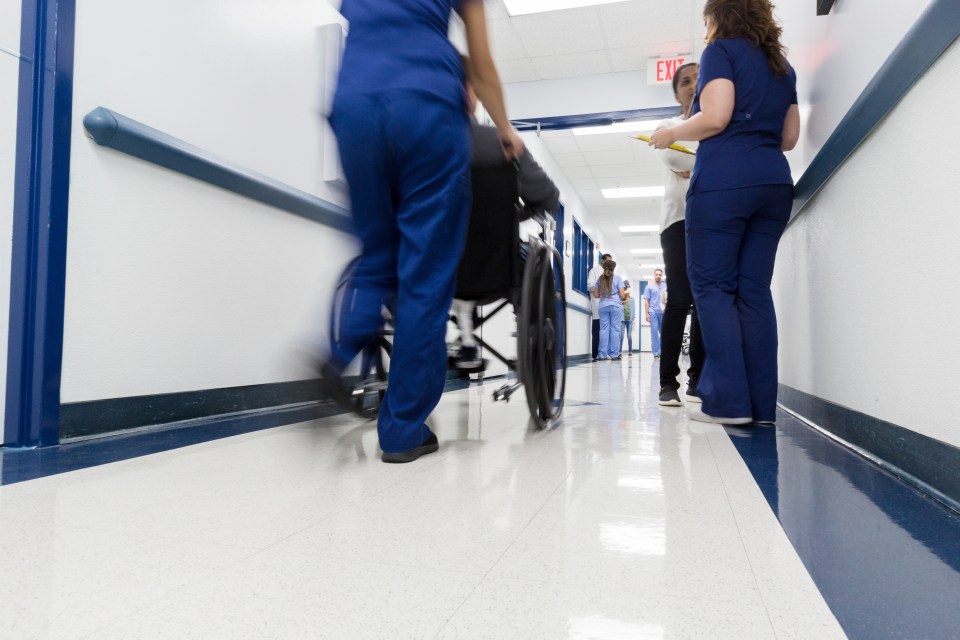 Nurse pushing a patient in a wheelchair down a hospital corridor.