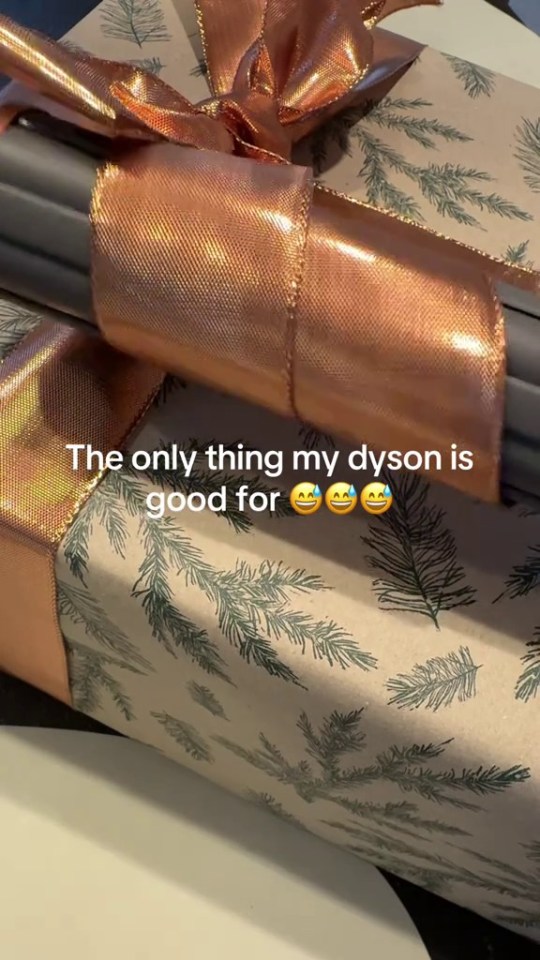 A Dyson hair curler used to curl a rose gold ribbon on a Christmas present.