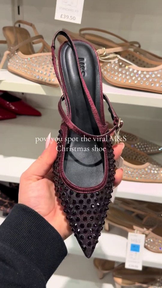 Close-up of a person holding a burgundy M&S Christmas shoe adorned with dark rhinestones.